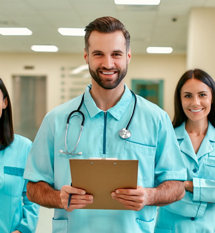 Smiling male doctor holding a clipboard with his team of doctors behind him